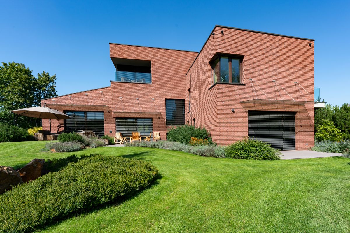 Een hedendaagse woning in rode baksteen met plat dak en een grote tuin.