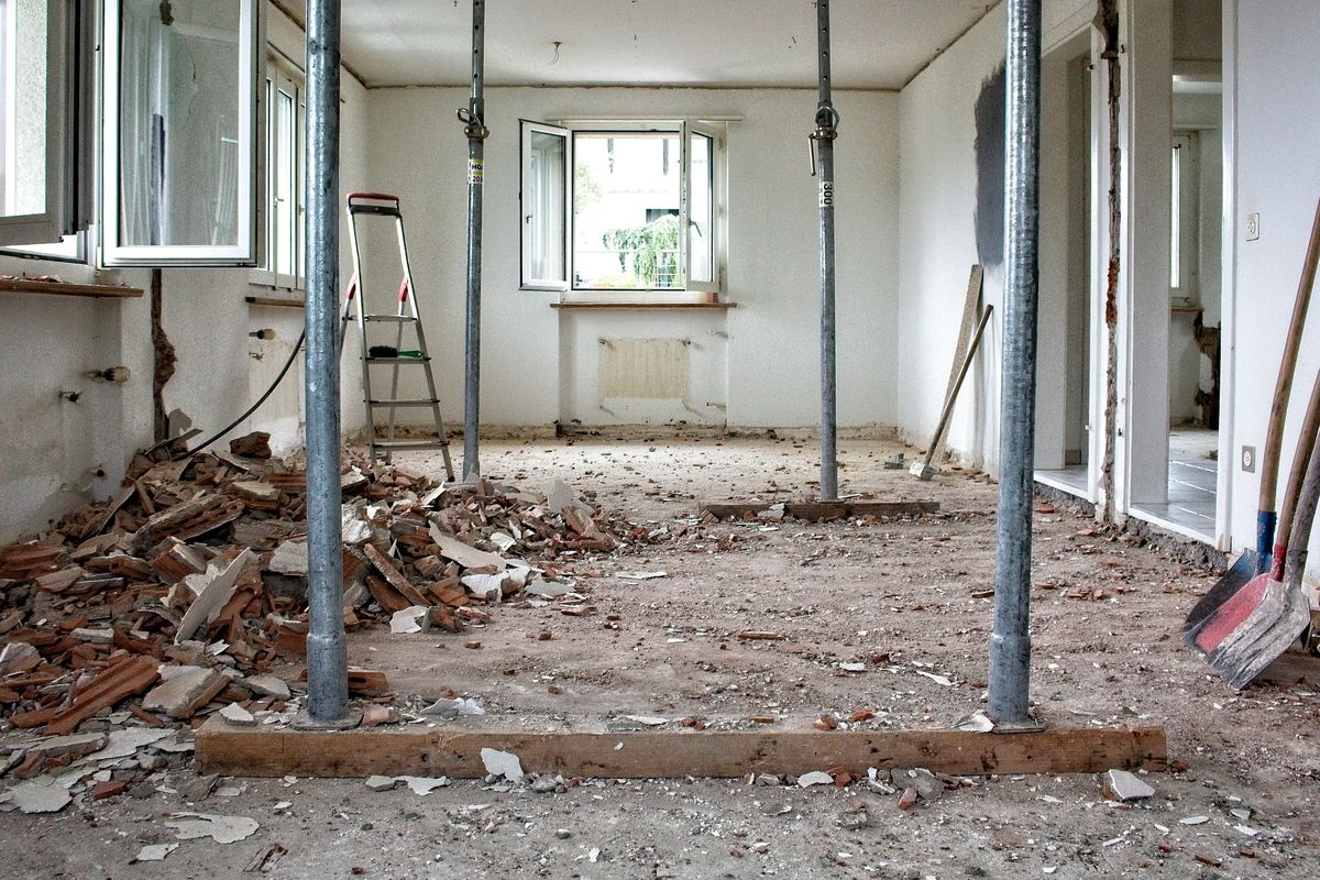 Een kamer in verbouwing: stalen stempels dragen het plafond, puin ligt op de vloer.